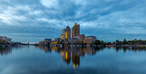 Reflection of buildings on lake against cloudy sky at dusk