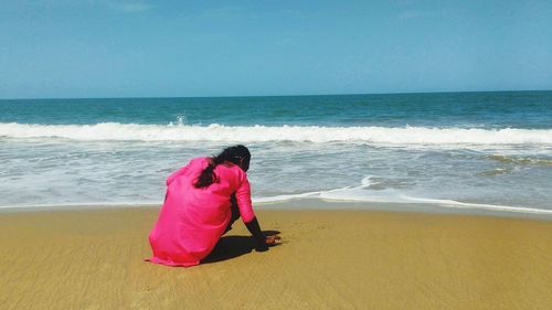 Rear view of woman standing at beach against clear sky