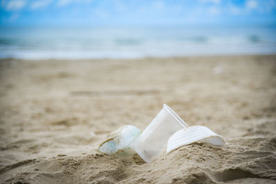 Close-up of paper bottle on sand at beach against sky