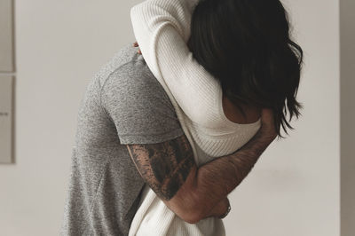 Romantic couple embracing while standing against wall at home