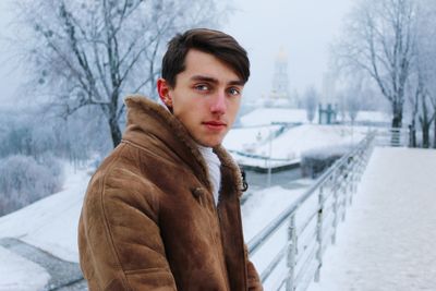 Portrait of young man standing by railing during winter
