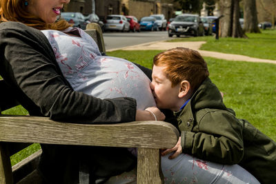 Side view of boy kissing pregnant mother abdomen at park