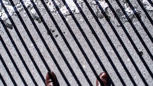 Low section of man standing on road with railing shadow