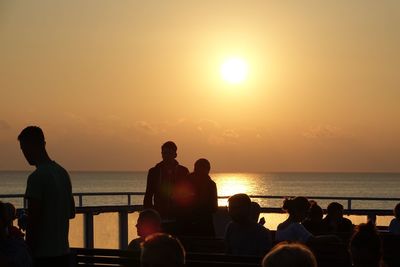Silhouette people sitting by sea against sky during sunset