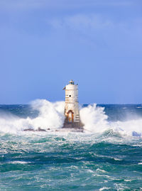 Lighthouse on sea by building against clear sky