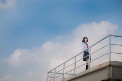 Low angle view of young woman wearing uniform while standing on balcony against sky