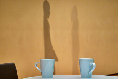 Close-up of coffee cup on table against wall and person shadows 