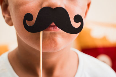 Midsection of boy holding mustache prop over lips