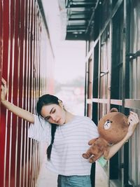 Young woman holding teddy bear while standing amidst walls