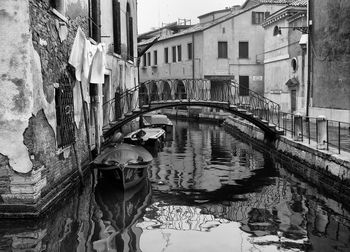 Rowboats moored on grand canal by arch bridge amidst old buildings