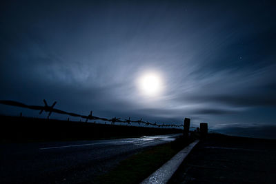Silhouette bridge over road against sky at dusk