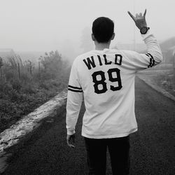Rear view of man gesturing on road during foggy weather