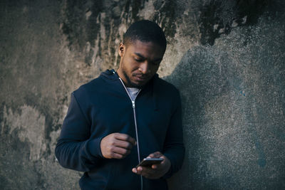 Young man leaning on wall while using smart phone