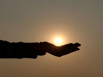 Close-up of silhouette hand holding sun during sunset