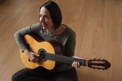 High angle view of woman playing guitar while sitting on floor at home