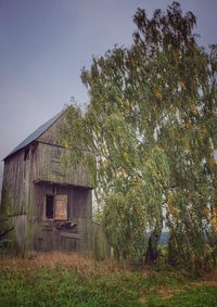 Abandoned house by trees on field against sky