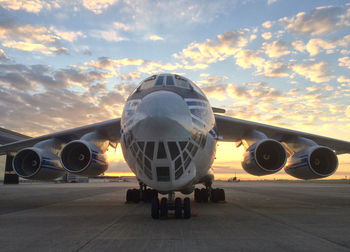 Airplane on airport runway against sky during sunset