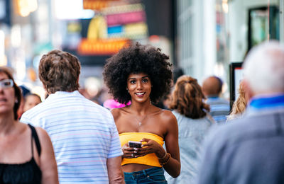 Portrait of happy young woman holding smart phone on city street