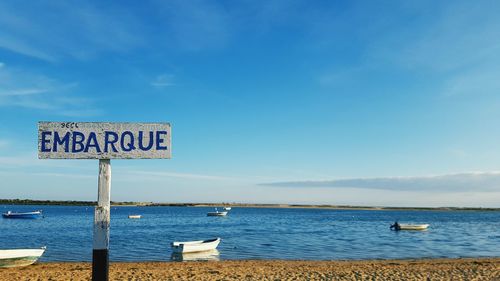 Information sign by sea against sky