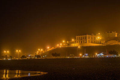 Illuminated buildings by sea against sky at night