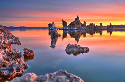 Reflection of rocks in sea against sky during sunset