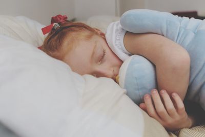 Close-up of girl embracing stuffed toy while sleeping on bed at home