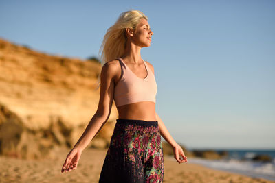 Young woman with eyes closed standing at beach against sky