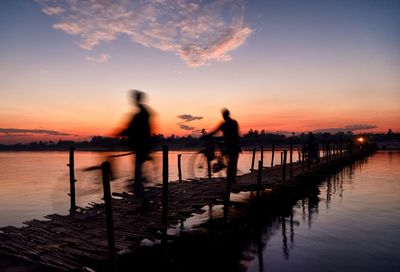 Silhouette people standing on pier over sea against sky during sunset