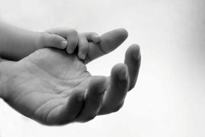 Close-up of parent and baby hand against white background
