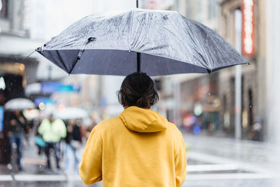 Rear view of woman with umbrella standing in rain