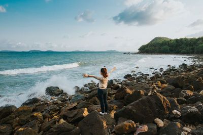 Rear view of woman standing on rock at beach against sky