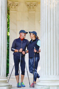 A man and woman with walking sticks and in sportswear take a break and look at each other