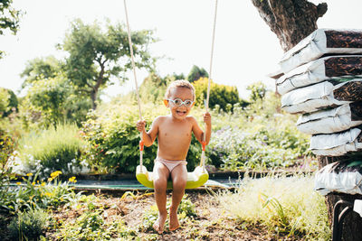 Portrait of shirtless boy sitting on swing against sky