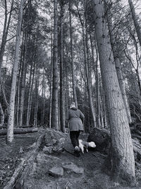 Rear view of woman walking a dog through apine forest