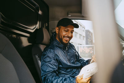 Smiling male delivery person holding parcel while sitting in van