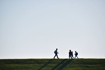 Family walking on field against clear sky