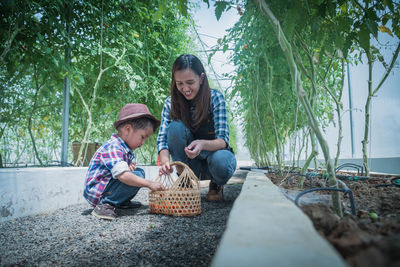 Full length of happy woman sitting by basket against trees