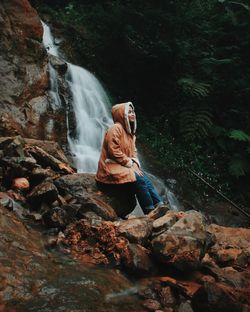 Full length of man sitting on rock in forest