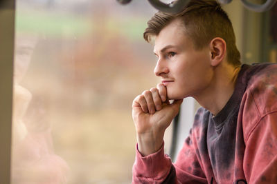 Side view of young man traveling by train, looks out of the window. blond man enjoying a train trip.