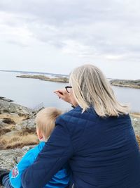 Rear view of woman sitting with grandson at beach against sky
