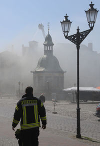 Rear view of firefighter walking on street against buildings in city