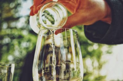 Cropped hand pouring water from jar in glass