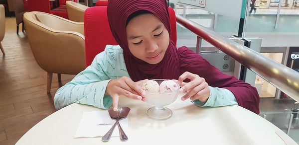 Girl in headscarf eating ice cream on table