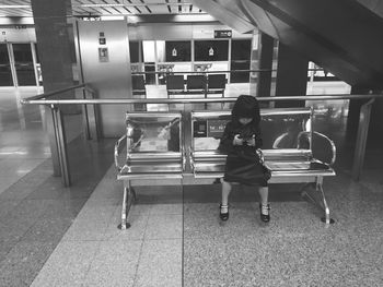 Full length of girl holding mobile phone on seat at railroad station