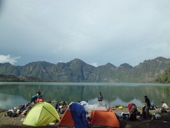 People on lake by mountains against sky