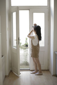 Side view of young woman photographing while standing at entrance