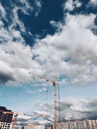 Low angle view of crane by building against sky