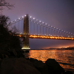 Illuminated bridge over river against sky at night