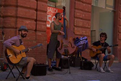 Street musicians playing guitar and violin on sidewalk against wall