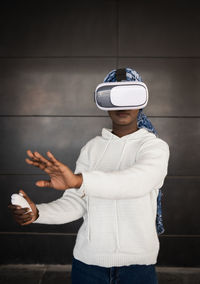 Concentrated young african american female millennial with headscarf in casual clothes pushing button of vr controller while experiencing virtual reality in modern headset